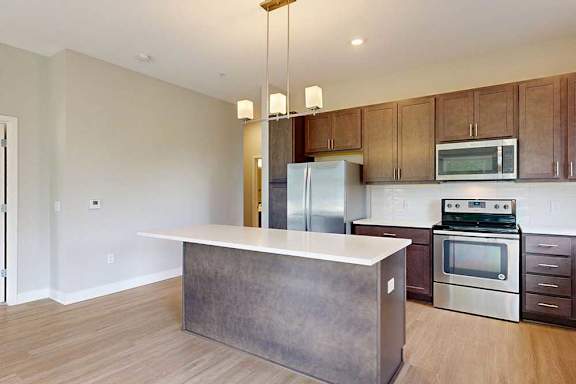 A kitchen with dark wood cabinets, quartz countertops, a large island, stainless steel appliances, and a designer backsplash.