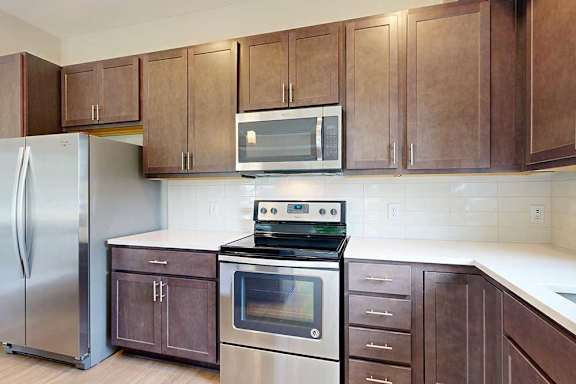 A kitchen with dark wood cabinets, quartz countertops, stainless steel appliances, and a designer backsplash.