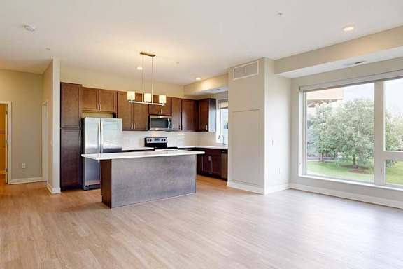 A living room with hardwood-style flooring and kitchen with dark wooden cabinets.