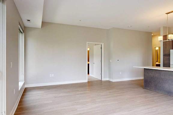A living room with hardwood-style flooring and kitchen with dark wooden cabinets.