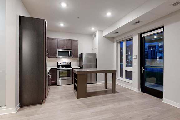 A living area with hardwood-style flooring and kitchen with dark wooden cabinets.