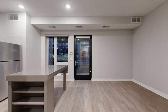 A kitchen island in front of a living area with hardwood-style flooring and floor-to-ceiling windows.