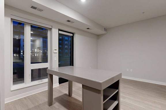 A kitchen island in front of a living area with hardwood-style flooring and floor-to-ceiling windows.