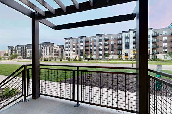 A patio with a black metal railing, a pergola covering, and a view of the neighborhood.