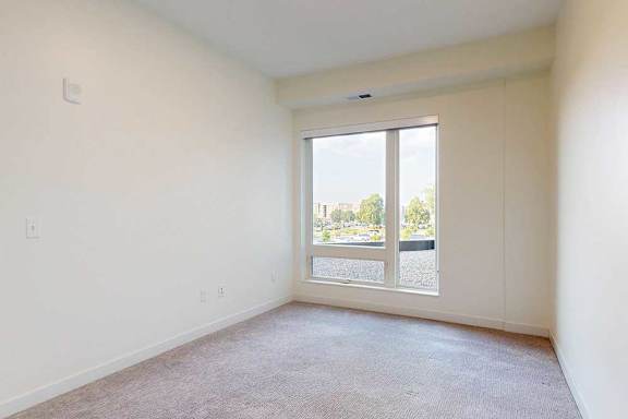 apartment bedroom with a large window and a carpeted floor.