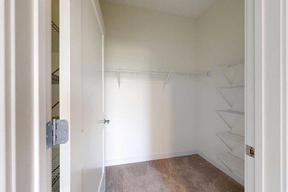 A walk in closet with a brown carpet and white wire shelves.