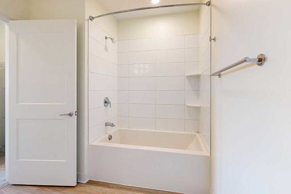 Minimalist bathroom with white tiles, a bathtub, and a showerhead. A towel bar is on the right wall.
