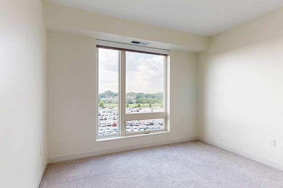 A carpeted bedroom with a window overlooking a parking lot.
