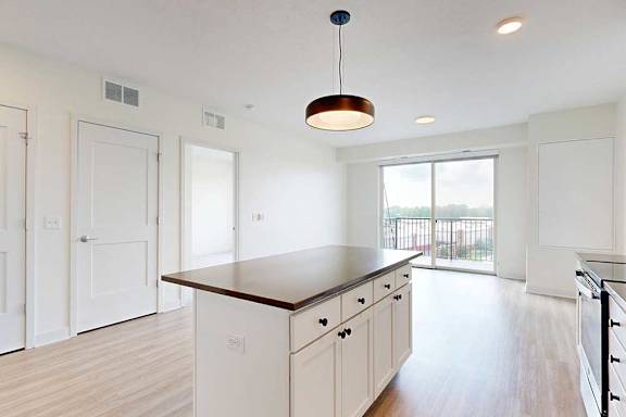 Modern kitchen with a central wooden island, white cabinets, and stainless steel appliances. Pendant light above island; large window shows balcony.
