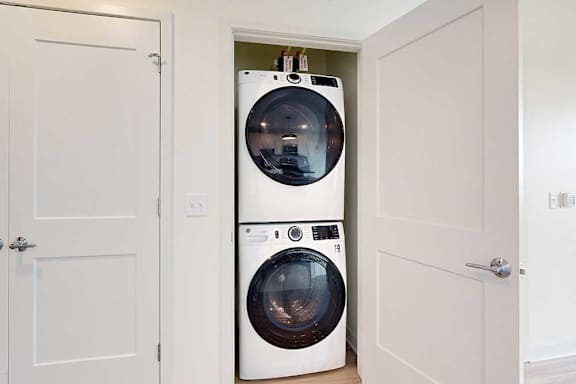 Two white front load washing machines in a small laundry closet