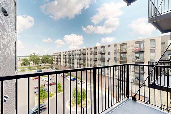 A balcony overlooks a parking lot and apartment building