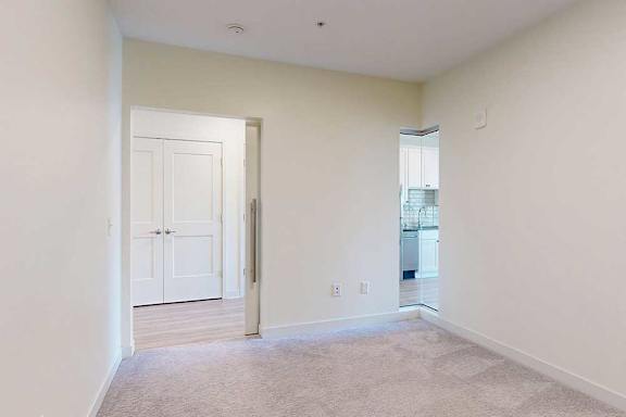 Carpeted sleeping area with pocket door and corner window looking to ktichen