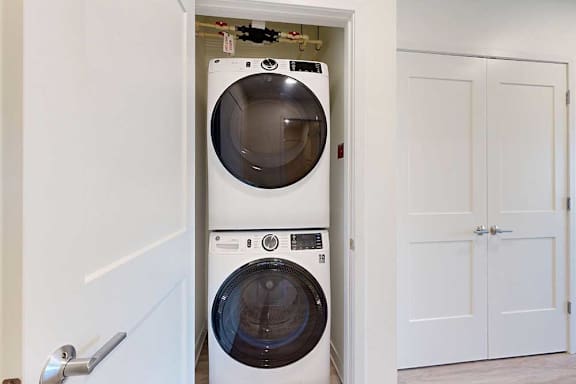 Stacked washer and dryer in a small, open closet with white doors, creating a compact and modern laundry space.