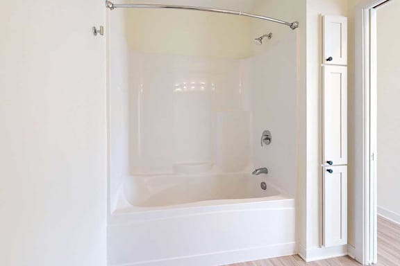 A clean, white bathroom featuring a bathtub with a shower, a curved curtain rod, and adjacent storage cabinets.