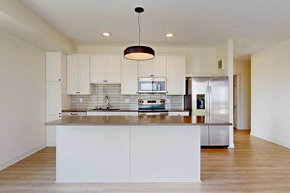 Modern kitchen featuring white cabinets, stainless steel appliances, and a spacious island with a sleek countertop and pendant lighting.