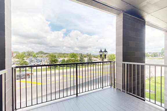 A balcony with a view of a parking lot and trees.