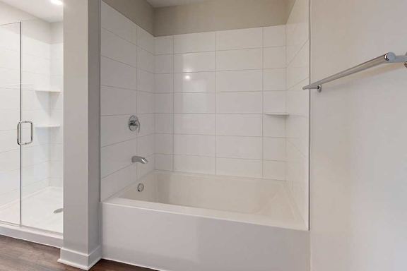 Modern bathroom with a white tiled bathtub and adjacent glass shower. A silver towel rack is on the right wall