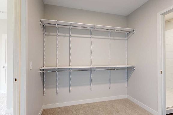 Empty closet with beige walls and carpet, featuring a simple white metal shelving unit attached to the wall.