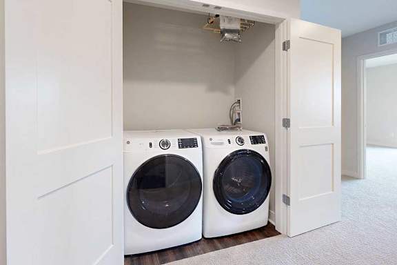Two white front loading washing machines in a closet with double doors
