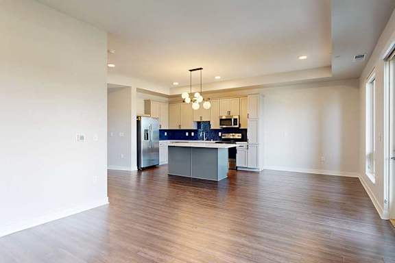 A spacious kitchen and living room area with a center island and pendant lights.