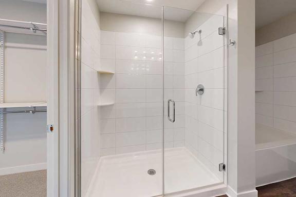 A white tiled shower with a glass door and a white tub next to it