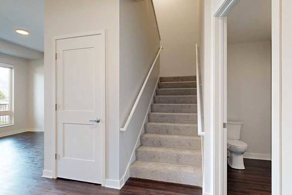 A modern interior with beige carpeted stairs, a white door to the left, and a bathroom with visible toilet to the right.