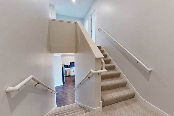 A staircase with a beige carpet and white railings.