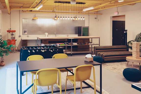 The bike lounge room with a foosball table, board games, a table with yellow chairs, and a striped sofa.