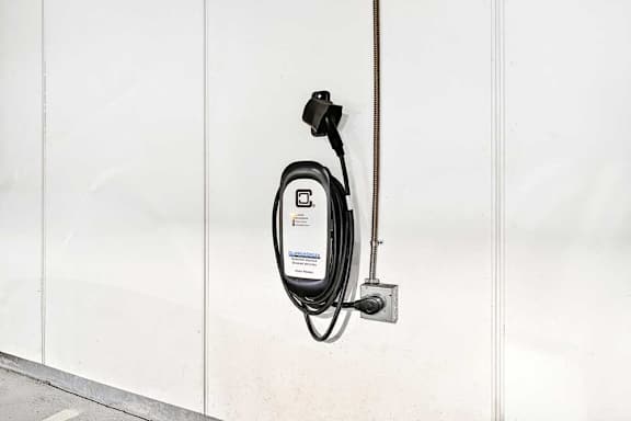 A black electric car charging cable plugged into a white wall socket.