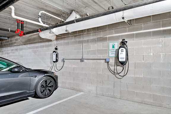 A grey car is charging at a wall-mounted charging station.