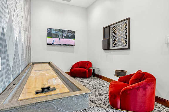 A room with a shuffleboard table and red chairs.