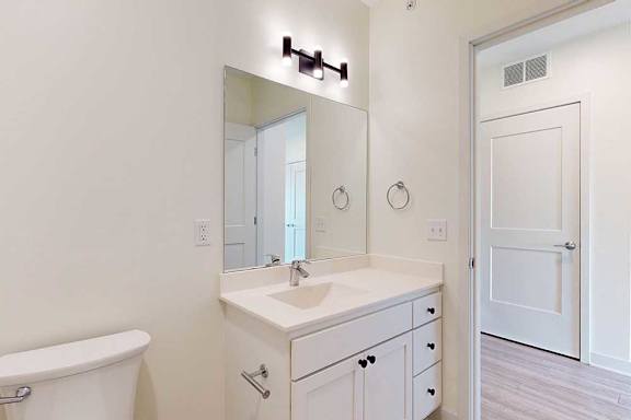 Modern bathroom with a clean, minimalist design. Features a large mirror, white vanity, sink, and a toilet.