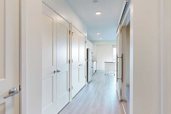 Bright, modern kitchen with sleek light wood flooring, white cabinets on the left, and stainless steel appliances.