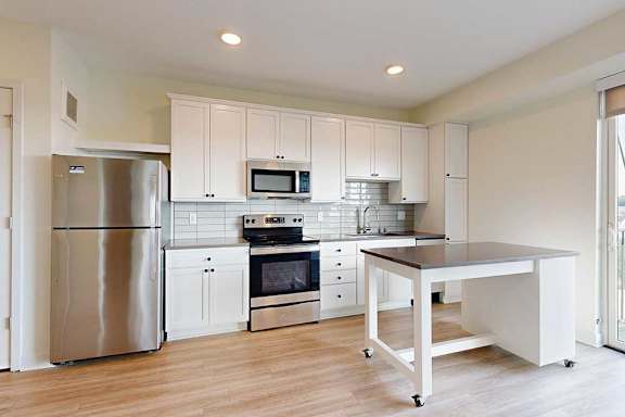 Bright, modern kitchen with white cabinets, a movable island, and light wood flooring. Large glass doors open to a balcony with a scenic view.