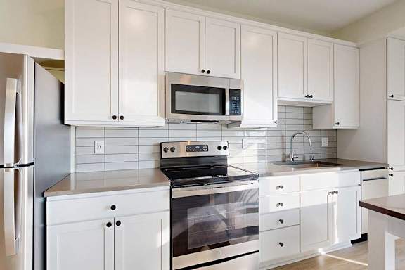 Modern kitchen with white cabinets, stainless steel appliances, including a fridge, oven, and microwave.