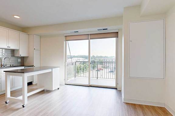 Bright, modern kitchen with white cabinets, a movable island, and light wood flooring. Large glass doors open to a balcony with a scenic view.