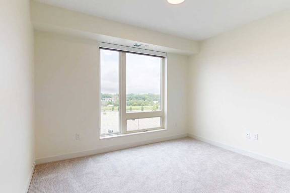 A large, empty bedroom with a window overlooking a parking lot.