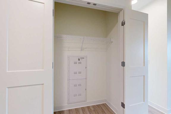 A white door is open to a hall closet with a white wall and a white shelf.