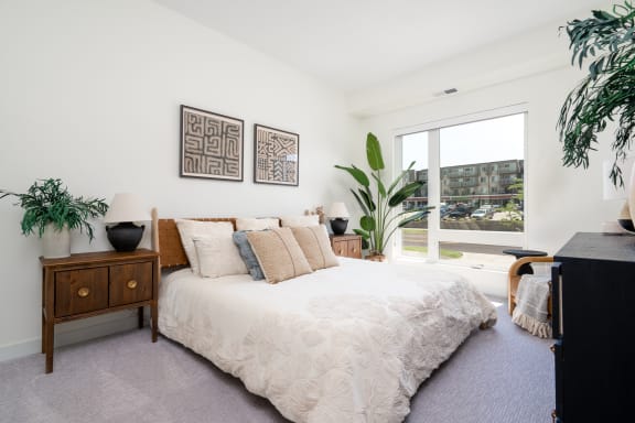 bedroom with king sized bed with off white linens , large window, and large plant in corner of room