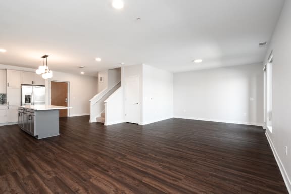 large open living and dining area with dark hardwood flooring. Kitchen counter and staircase to the left.