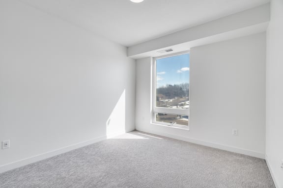 Spacious carpeted bedroom with large window allowing a lot of natural light in at The Rowan apartments