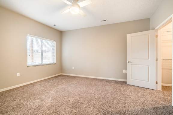 A room with a carpeted floor, a ceiling fan, and a door.