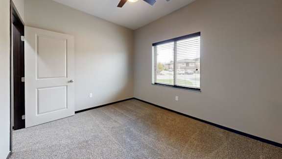 A room with a white door, carpeted floor, and a window with blinds.