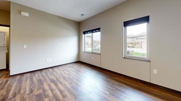 A living  room with wooden flooring and two windows.