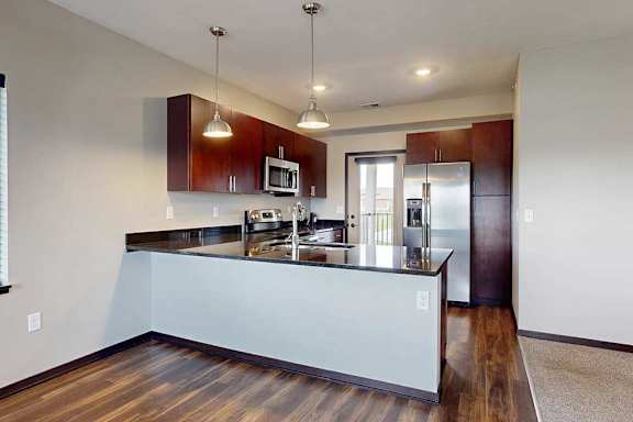 A kitchen with dark wooden cabinets, granite countertops, stainless steel appliances, and a peninsula countertop.