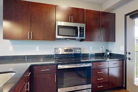 A kitchen with dark drown cabinets, granite countertops, and a stainless steel microwave and range.