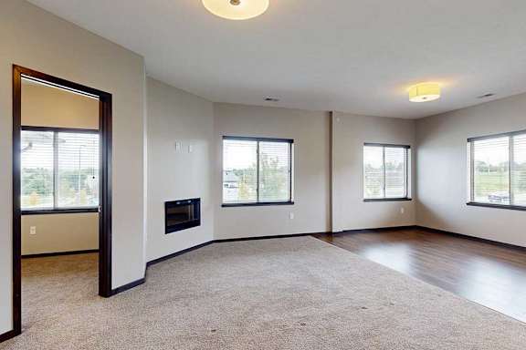 A carpeted living room with several windows, an electric fireplace, and an open door to a den space.