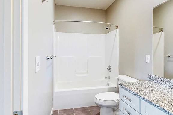 A bathroom with a granite vanity, white wooden cabinets, and a tub shower.