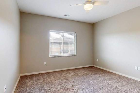A carpeted bedroom with a ceiling fan and a window.