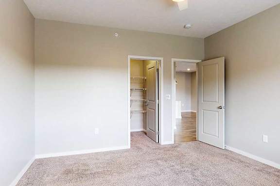 A carpeted bedroom with a walk-in closet and a door open to the living room.